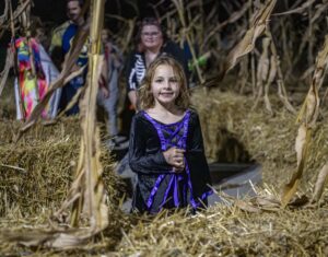 Young girl dressed in costume standing in the middle of a hay maze