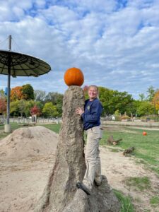 Zookeeper Ashley standing on a tree trunk and holding a pumpkin