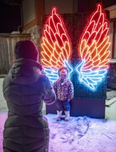 A little girl posing in front of giant illuminated wings
