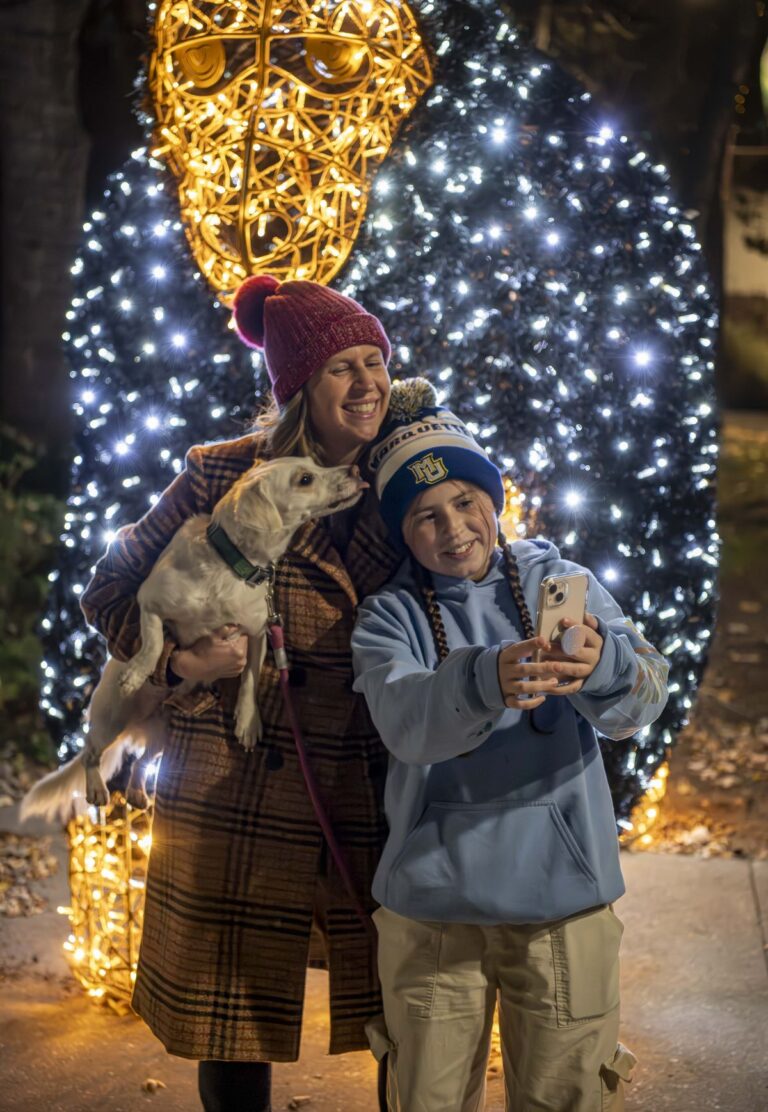 Family taking a selfie photo with their dog in front of an illuminated gorilla sculpture