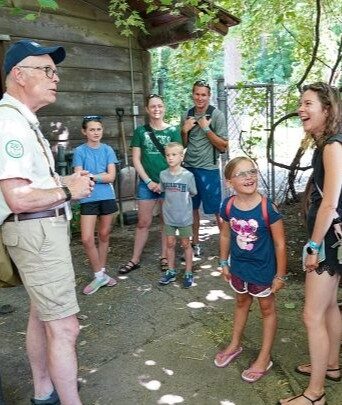 Group of adults and kids standing in front of an outdoor animal habitat with a tour guide